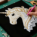 Handmade unicorn design with beads and lace on a black background, with a hand using a pink tool.