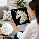 Woman holding a completed unicorn pearl painting with decorative elements on a couch.