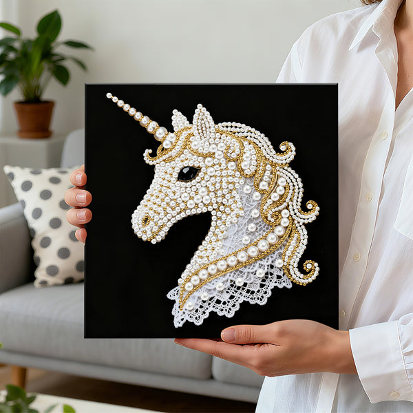 Person holding a black square with a decorative unicorn design made of pearls and gold elements.