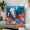 Person holding a completed diamond painting of an underwater scene with jellyfish, starfish, and corals.
