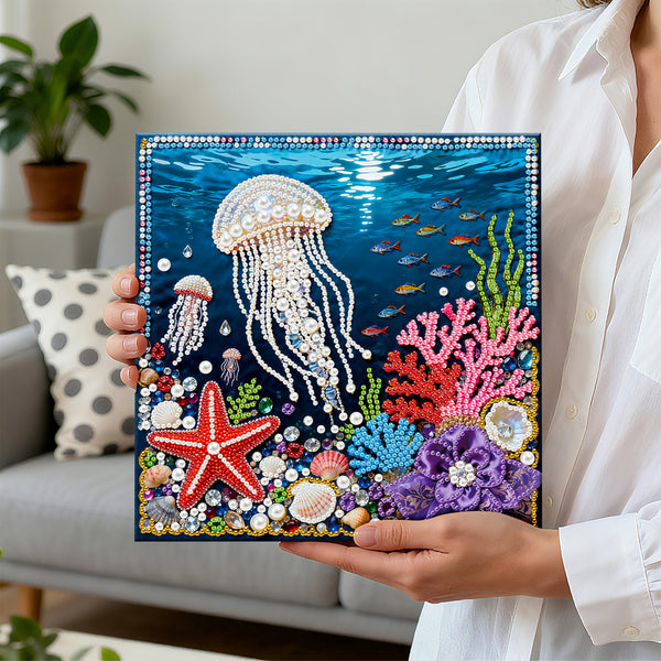 Person holding a completed diamond painting of an underwater scene with jellyfish, starfish, and corals.