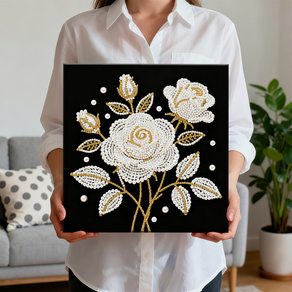 Person holding a decorative painting with white and gold floral design on a black background.