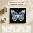 Butterfly art piece with pearl inlay on a wooden surface with a cup and plant.