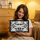 Woman holding a black frame with white decorative pearl painting of a dragonfly and flowers.