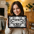 Woman holding a decorative pearl painting with a dragonfly design in a cozy living room.