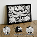 Decorative wall art with a dragonfly design on a black background, displayed on a wooden surface.