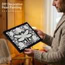 Man holding a black canvas with white decorative pearl painting of a dragonfly and flowers.