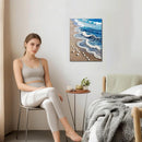 Woman sitting on a chair in a bedroom with a beach scene painting on the wall.
