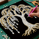 Hand applying gold and pearl decorations to a tree design on black paper with a pink pen.
