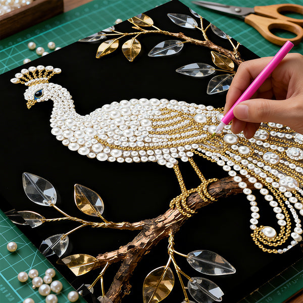 Handmade peacock design with pearls and gold accents on a black background, with a hand using a pink tool.