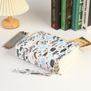 A hardcover notebook with a white cover decorated with a colorful botanical leaf pattern, shown on a white desk next to a pleated lamp, colored pencils, and books.