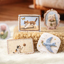 Collection of embroidered items featuring cats and birds on a textured surface.