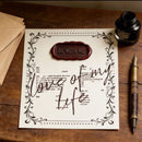 Invitation card with 'Be with me' and 'love of my life' text on a wooden surface with envelopes and an inkwell.