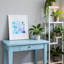 Blue table with a framed artwork and plants in a room setting