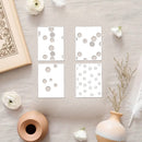 Four white cards with gray circular patterns on a light wooden surface with decorative items.