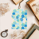 Notebook with blue and green circular pattern on a white surface with books and flowers.