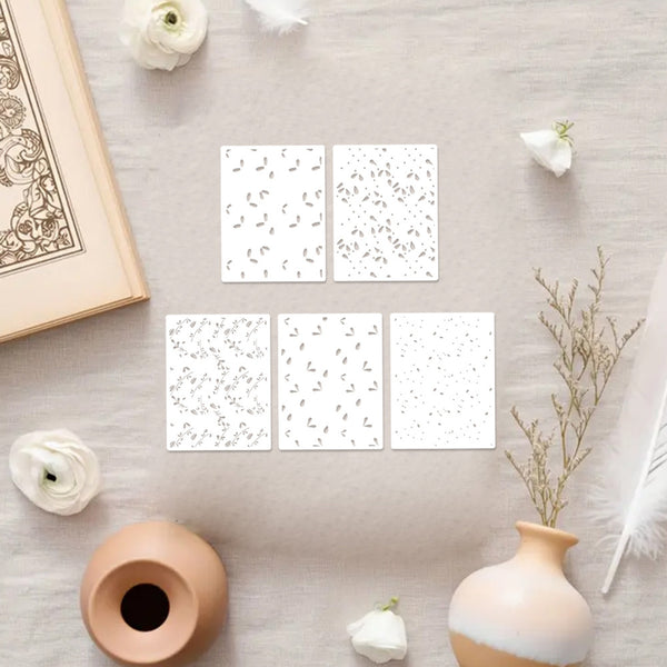Set of six white cards with floral patterns on a light wooden surface with decorative items.