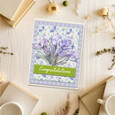 Greeting card with purple crocus flowers and 'Congratulations' text on a wooden surface with flowers and books.