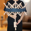 A person wearing a black shirt holds a wooden spinning wheel with a blue yarn wrap around it, set against a softly blurred indoor background.
