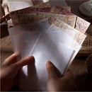 Hands holding a stack of vintage-style cards and envelopes on a wooden surface.