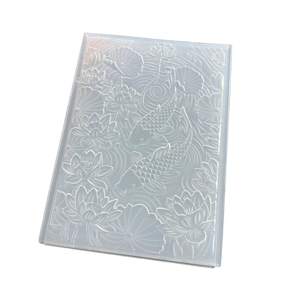A rectangular translucent plastic mold or stamp with an embossed koi fish and lotus pond design, shown on a plain white background.