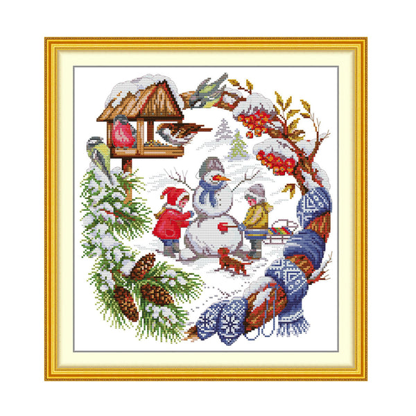 Cross-stitched scene with children making a snowman, framed in gold.