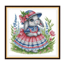 Cross-stitched design of a rabbit in a dress and hat with flowers and grass.