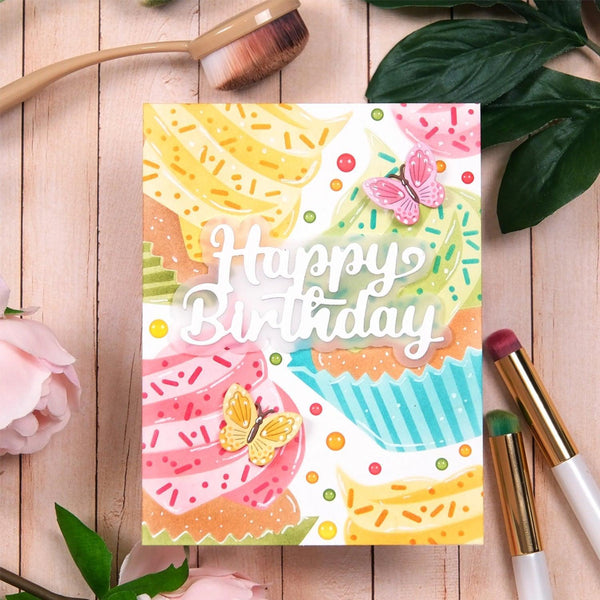 Colorful birthday card with pastel-colored treats and 'Happy Birthday' text on a wooden surface with makeup items.