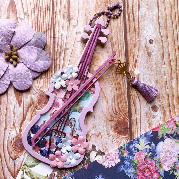 Decorative keychain shaped like a violin with floral elements on a wooden surface.