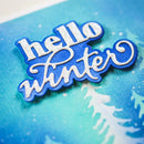 Decorative cutout with 'hello winter' text on a blue background with snowflakes and tree silhouettes.