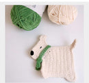 Crocheted dog toy with green scarf next to green and beige yarn on a light background