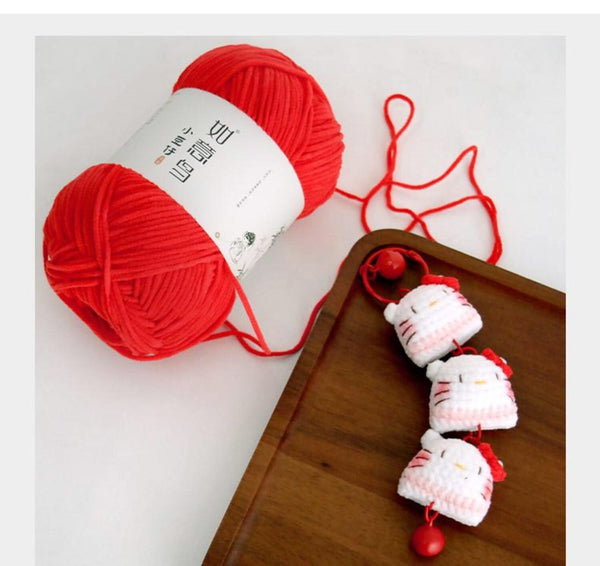 Red yarn ball with a white label next to a small crocheted cat toy on a wooden surface.