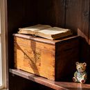 Wooden box with an old book on top, next to a small bear figurine on a wooden shelf.