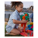 Child playing with crocheted carrots on a grassy area by a lake.