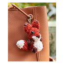 Crocheted fox keychain attached to a brown leather bag with a blurred natural background.