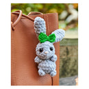 Gray bunny plush toy with a green bow on a brown leather bag
