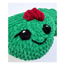 Close up of Green plush Holly Jolly Holly amigurumi with a red bow on a white background