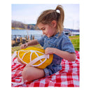 Child holding a yellow plush toy on a red and white checkered blanket by a lake.