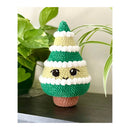 Crocheted Christmas tree ornament with a face on a wooden surface with plants in the background