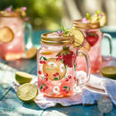 Pink lemonade in a mason jar with floral design on a blue table outdoors.