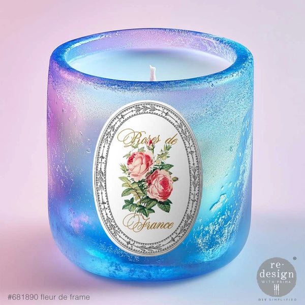 Candle in a blue glass holder with a floral label on a light purple background