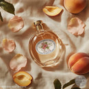 Perfume bottle with floral label surrounded by peach slices and petals on a textured surface