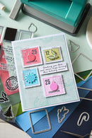 Card with postage stamp designs on a crafting table with stamps and dies.