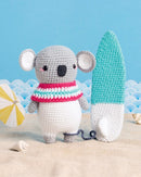 Crocheted koala and gnome on a beach with a blue sky background