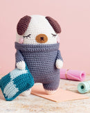Crocheted dog toy with a sweater on a wooden surface with crafting materials.