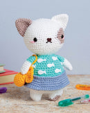 Crocheted cat toy with a green sweater and orange bag on a wooden surface.