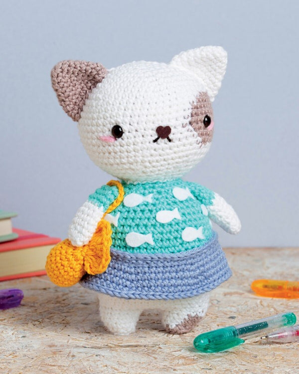 Crocheted cat toy with a green sweater and orange bag on a wooden surface.