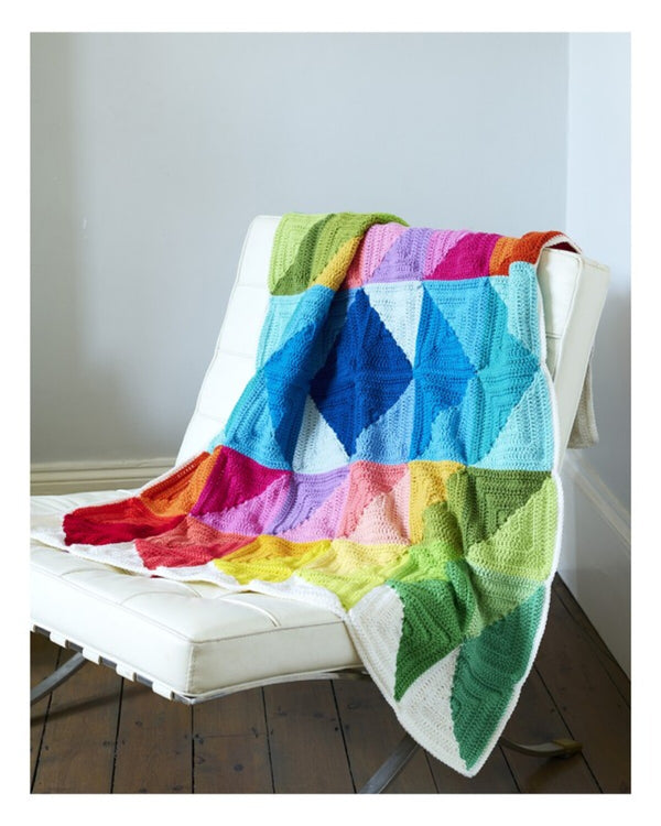 Colorful knitted blanket draped over a white chair against a plain wall.