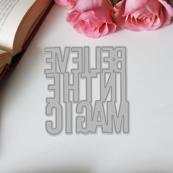 Metallic bookmark with 'Believe in the Magic' text on a white surface with pink roses and an open book.