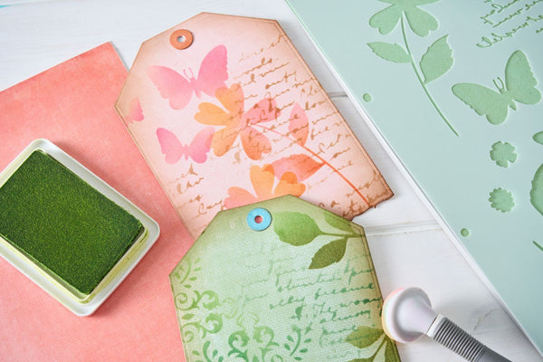 Decorative tags with floral designs and a green stamp pad on a white surface.